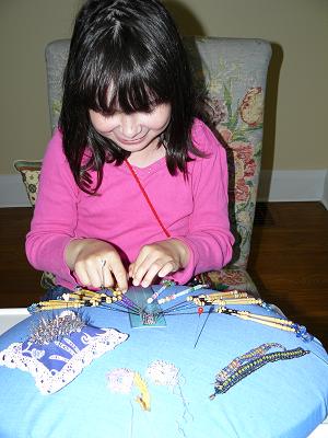 Girl sitting doing bobbin lace with beads - 2