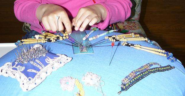 Girl sitting doing bobbin lace with beads - close-up